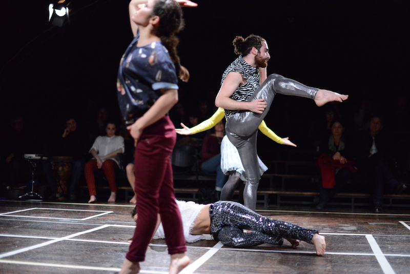 Dancers perform a grided stage and wear shiny pants